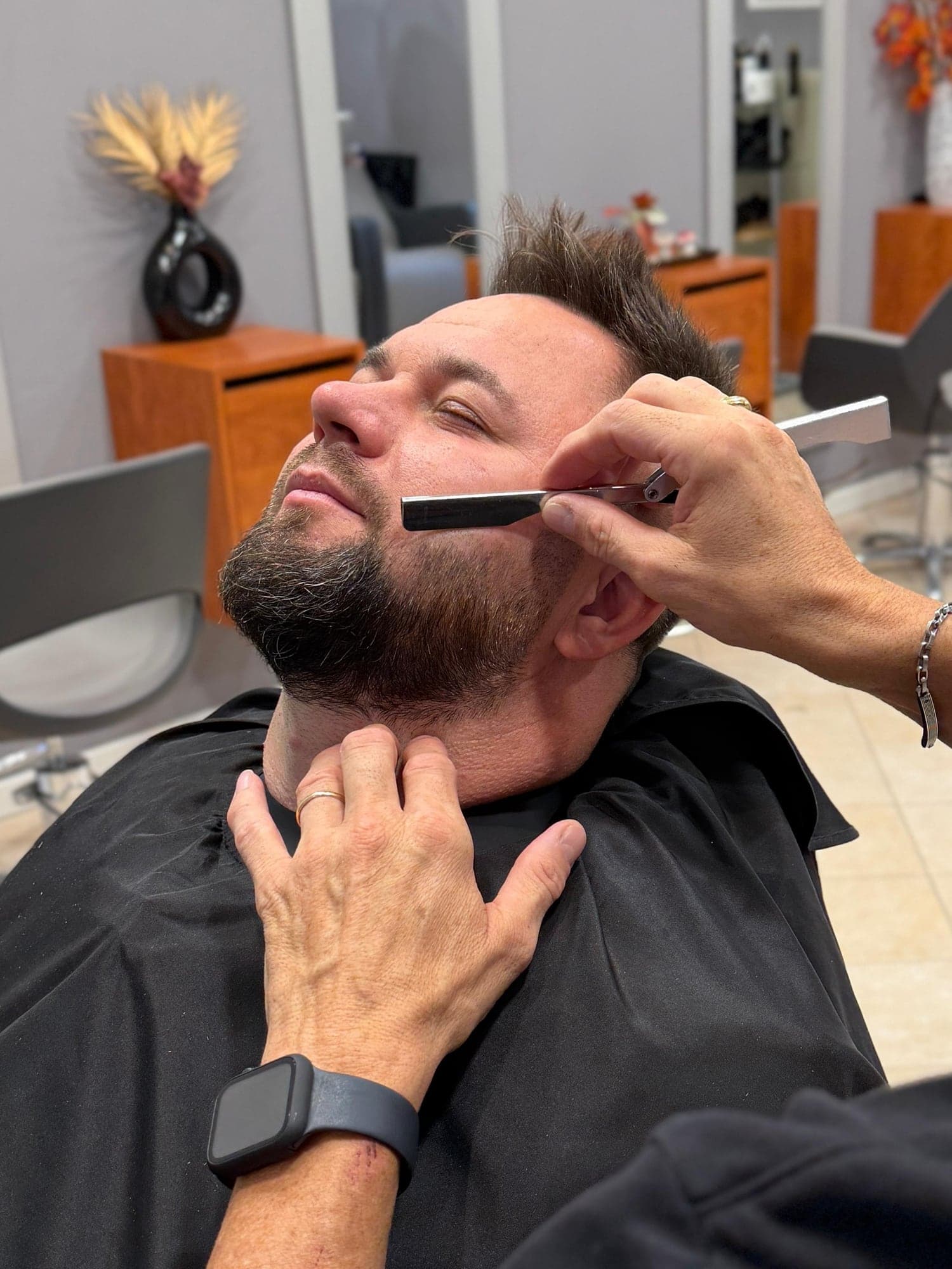Rifinitura dei contorni della barba con rasoio, cliente in poltrona